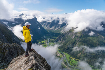 Obraz premium Young Asian man traveller standing on rock looking to mountains, Romsdalseggen hiking trail, Norway, Scandinavia