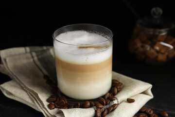 Delicious latte macchiato and coffee beans on black table