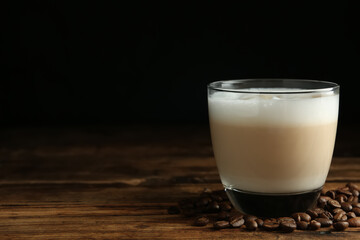 Delicious latte macchiato and coffee beans on wooden table against black background, space for text