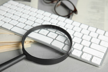 Magnifying glass, keyboard and stack of newspapers on grey table, closeup. Job search concept