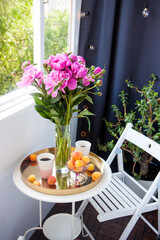 Summer breakfast on balcony. Two cups of drink, bouquet of pink peonies, old book and fresh fruits on white table.