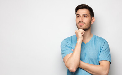 Banner of young man in blue t-shirt with dreamy cheerful expression, thinking, isolated on gray background with copy space for your ads
