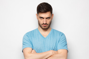 Young aggressive man standing with arms crossed and serious concentrated face, isolated on gray background