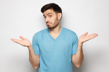 I don't know. Portrait of young confused man in blue t-shirt standing and shrugging shoulders,...