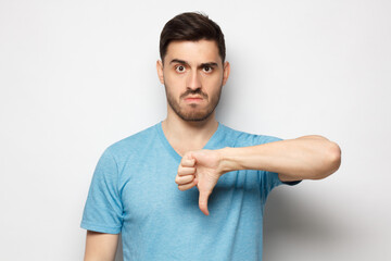 Young dissatisfied man showing thumb down or dislike, isolated on gray background