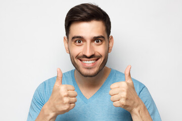 Young happy man showing thumbs up isolated on gray background