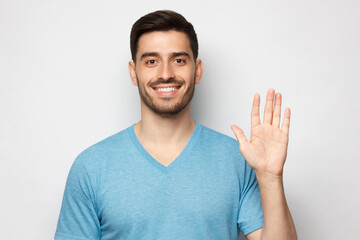 Young smiling man greeting someone with open hand, wearing blue tshirt, isolated on gray background