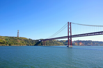 Fototapeta premium Wiszący most 25 de Abril łączący Lizbonę z gminą Almada i posąg Chrystusa w tle nad ujściem rzeki Tejo w Lizbonie w Portugalii.