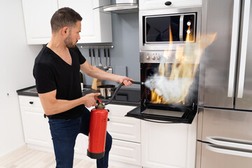Man Using Fire Extinguisher To Put Out Fire From Oven