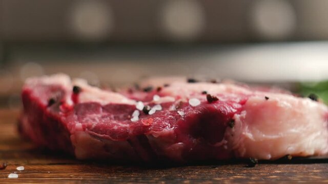 Extreme Close Up view of juicy raw steak meat being salted and spiced, garnished. Seasoning fresh steak in a bright light. Cuisine, bon appetite, pepper salt, garlic and rosemary, Modern Cuisine.