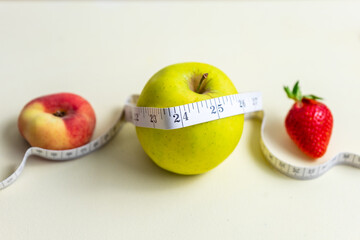 Ein Apfel, ein Pfirsich und eine Erdbeere mit einem Massband auf einem gelben Hintergrund, Diät, Gesundheit, gesunde Ernährung