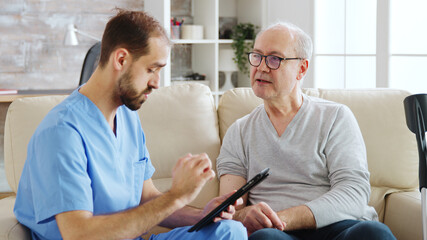 Caucasian male nurse talking with a nursing home patient about his health. The nurse is making...
