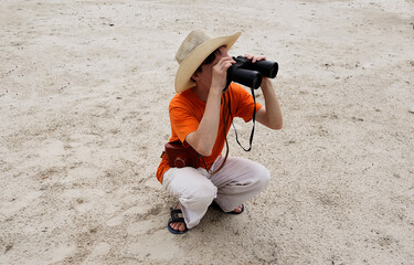 Obraz premium The young man looks through binoculars, squatting down.