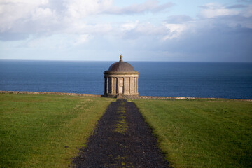 Museenden Temple Ireland auf der wiese mit meer im Hintetgrund und blauem himmel im Sonnenlicht