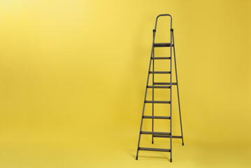 Metal stepladder on yellow background. Space for text