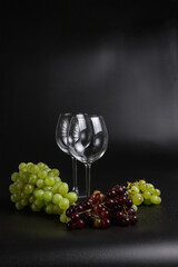 Still life on a black background. A glass wine glass and grape vine.