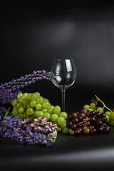 Still life on a black background. A glass wine glass and grape vine. Lupins on the black.