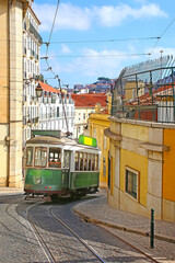 Fototapeta na wymiar Historic green tram against old town streets, part of the tramway network since 1873, Lisbon, capital city of Portugal.