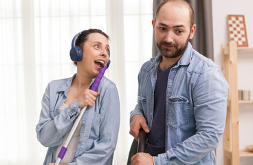 Husband ignoring wife while he's trying to clean the floor with vacuum cleaner.