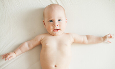 Cute baby lies on a white sheet and plays fun