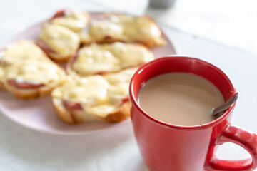 A cup of coffee and homemade hot sandwiches with sausage and melted cheese on pink plate for breakfast in the morning. Close-up.