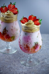 Cold summer dessert. Bowls of layered jelly served on table against light background. Colourful, festive cocktail with sweets jelly in glass. Strawberries, yogurt and chocolate cream close-up.