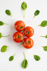 Sprig of fresh red juicy tomatoes in the center and leaves of spinach around it on a white table. Vegeterian food. Vertical. Close-up. Top view