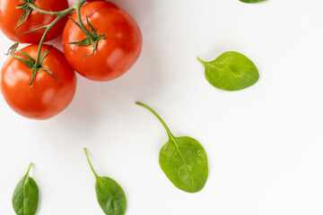 Sprig of fresh red juicy tomatoes in the upper left corner and leaves of spinach around it on a white table. Vegeterian food. Top view. Close-up
