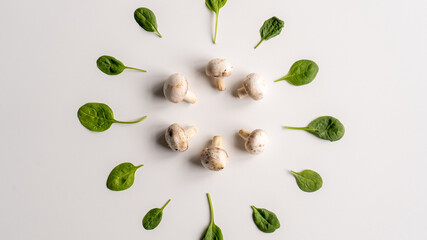 Fresh hampignons and spinach leaves in the center of a white background. Healthy food for diet. Top view. Close-up