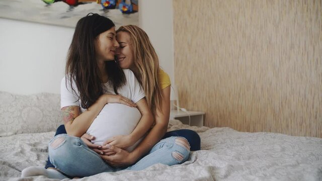 Portrait of happy lgbt lesbian family expecting a baby. Mixed race women in love, petting a big belly. Happiness of motherhood. IVF, LGBTQI, LBGT Pride Month, relationship, childbirth concept.