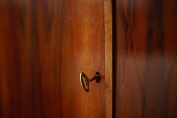 old key sticks out in the keyhole of a brown lacquered chest door