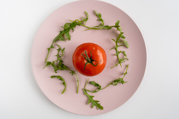Fresh green arugula leaves and tomato on a pink plate on a white table. Healthy diet. Top view. Close-up