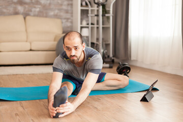 Man with healthy body doing legs stretching on yoga mat in home during covid-19 lockdown.