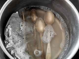 workshop for cleaning tarnished silver with aluminum foil and baking soda - top view of silver teaspoons in boiling solution of baking soda with aluminum foil in pot on electric stove