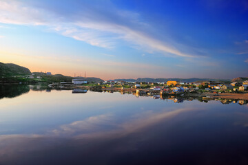 Summer evening in Teriberka, Murmansk oblast, Kola peninsula, Northern Russia. Beautiful nature scenery, sunset sky with cloud reflected in smooth surface of calm water, surf, wooden houses and boats