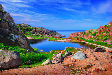 Way to waterfall in Teriberka, Murmansk oblast, Kola peninsula, Northern Russia. Awesome nature scenery, colorful rocks, green moss, lake and Barents Sea at the background of blue sky