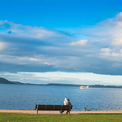 A father and a child sitting on a lakeside bench and watching a seaplane speeding up to take off from the lake Rotorua