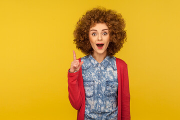 Eureka, I know answer! Portrait of amazed inspired woman with curly hair pointing finger up and having genius idea, surprised by sudden clever solution. studio shot isolated on yellow background - obrazy, fototapety, plakaty