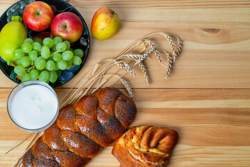 Wicker bun, lemon, apples, green grapes, wheat and a glass with milk on a wooden table. Jewish holiday Shavuot.