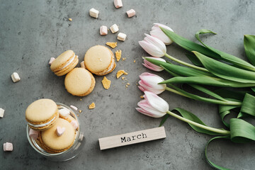 Fototapeta na wymiar Flat Lay Background of Fresh Tulips, Yellow French Macarons and Calendar March on the Table