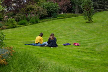 two young women sitting on grass, rear view, girl frends together, students