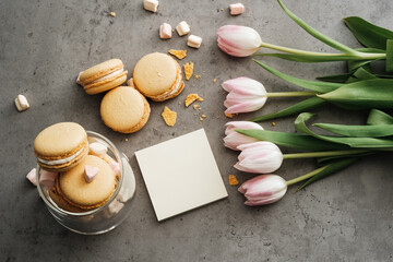 Fototapeta na wymiar Flat Lay Background of Fresh Tulips, Yellow French Macarons and Empty Note on the Table, Copy Space