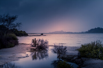 Fototapeta na wymiar Dramatic sunset over lake Rotorua on a rainy day. Coastline shrubbery over rocks.