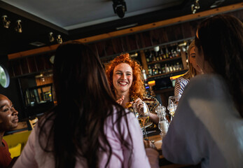 Fototapeta premium Group of young female friends having fun in restaurant, talking and laughing while dining at table.
