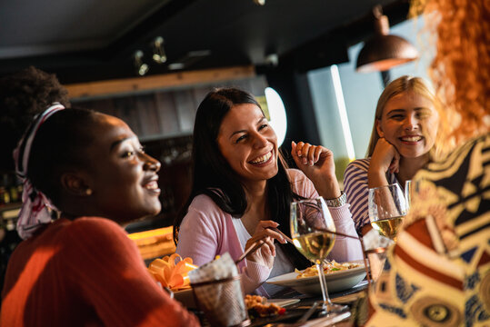 Group of young female friends having fun in restaurant, talking and laughing while dining at table.
