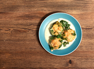 baked meatballs in spinach sauce with cheese on a wooden table in a plate