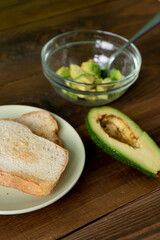 Fried bread for toasts and avocado for breakfast in the morning on brown woodwn table on green background.  Vretical
