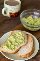 Tasty toasts with avocado and a cup of coffee for breakfast on plate on brown wooden table. Vertical. Close-up