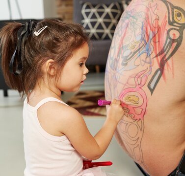 Little girl playing colouring her father's back. 