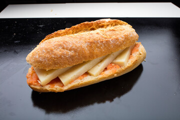 bocadillo, baguette con tomate y queso sobre fondo negro. sandwich, baguette with tomato and cheese on a black background.